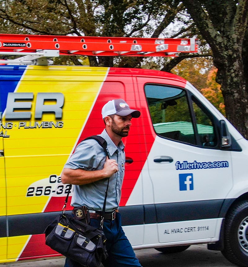 HVAC technician walking with a tool bag beside a brightly wrapped Fuller service van.