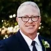 Headshot of Randal, Owner of Fuller, smiling in glasses wearing a suit outdoors.