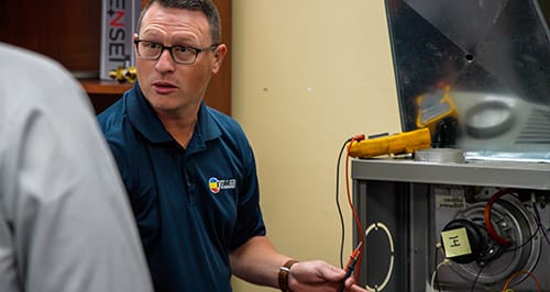 Fuller HVAC technician inspecting and testing furnace electrical components indoors.
